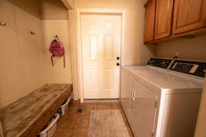 Washroom featuring washing machine and clothes dryer, cabinet space, and light tile patterned flooring