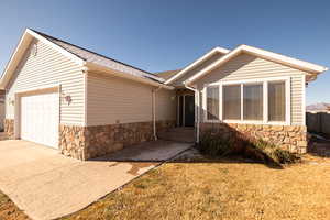 View of front of property featuring stone siding, driveway, an attached garage, and a shingled roof