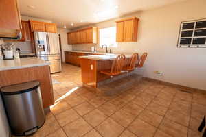 Kitchen featuring a peninsula, light tile patterned floors, light countertops, stainless steel refrigerator with ice dispenser, and a kitchen bar