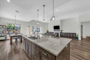 Kitchen featuring dark brown cabinetry, ceiling fan, a stone fireplace, light stone counters, and open floor plan