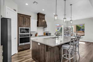 Kitchen featuring dark brown cabinets, light stone countertops, appliances with stainless steel finishes, an island with sink, and a breakfast bar area