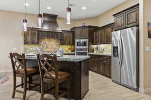 Kitchen with appliances with stainless steel finishes, dark brown cabinetry, a kitchen island with sink, a kitchen breakfast bar, and recessed lighting