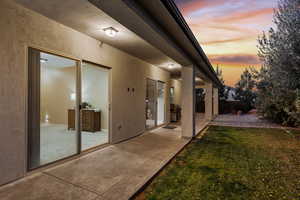 Doorway to property featuring a lawn, a patio, and stucco siding
