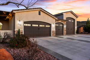 View of front of house with stone siding, stucco siding, concrete driveway, and a garage