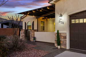 View of exterior entry with stone siding, stucco siding, a gate, a garage, and covered porch