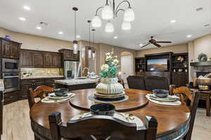 Dining space with arched walkways, a ceiling fan, light wood-type flooring, recessed lighting, and a fireplace