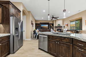 Kitchen featuring dark brown cabinetry, stainless steel appliances, a stone fireplace, light stone countertops, and decorative light fixtures