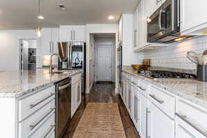 Kitchen featuring white cabinets, decorative light fixtures, dark wood finished floors, light stone counters, and recessed lighting