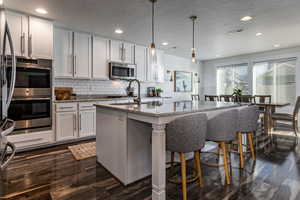 Kitchen with white cabinets, a textured ceiling, an island with sink, appliances with stainless steel finishes, and light stone counters