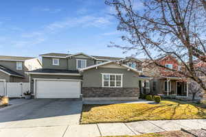 Traditional home with stucco siding, driveway, a garage, stone siding, and a gate