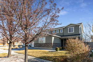 View of front facade featuring stone siding, stucco siding, driveway, a front yard, and a garage