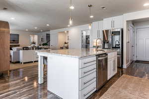 Kitchen featuring open floor plan, white cabinetry, an island with sink, a textured ceiling, and a kitchen breakfast bar