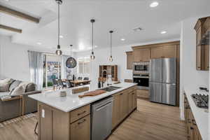 Kitchen featuring appliances with stainless steel finishes, open floor plan, pendant lighting, brown cabinetry, and light wood-type flooring