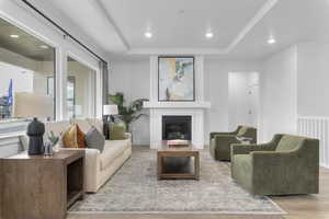 Living area with a tray ceiling, recessed lighting, a glass covered fireplace, and light wood-style flooring