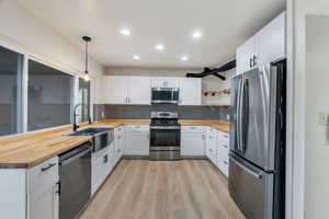Kitchen featuring open shelves, white cabinetry, appliances with stainless steel finishes, hanging light fixtures, and recessed lighting