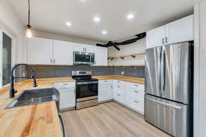 Kitchen with appliances with stainless steel finishes, open shelves, white cabinets, butcher block countertops, and hanging light fixtures