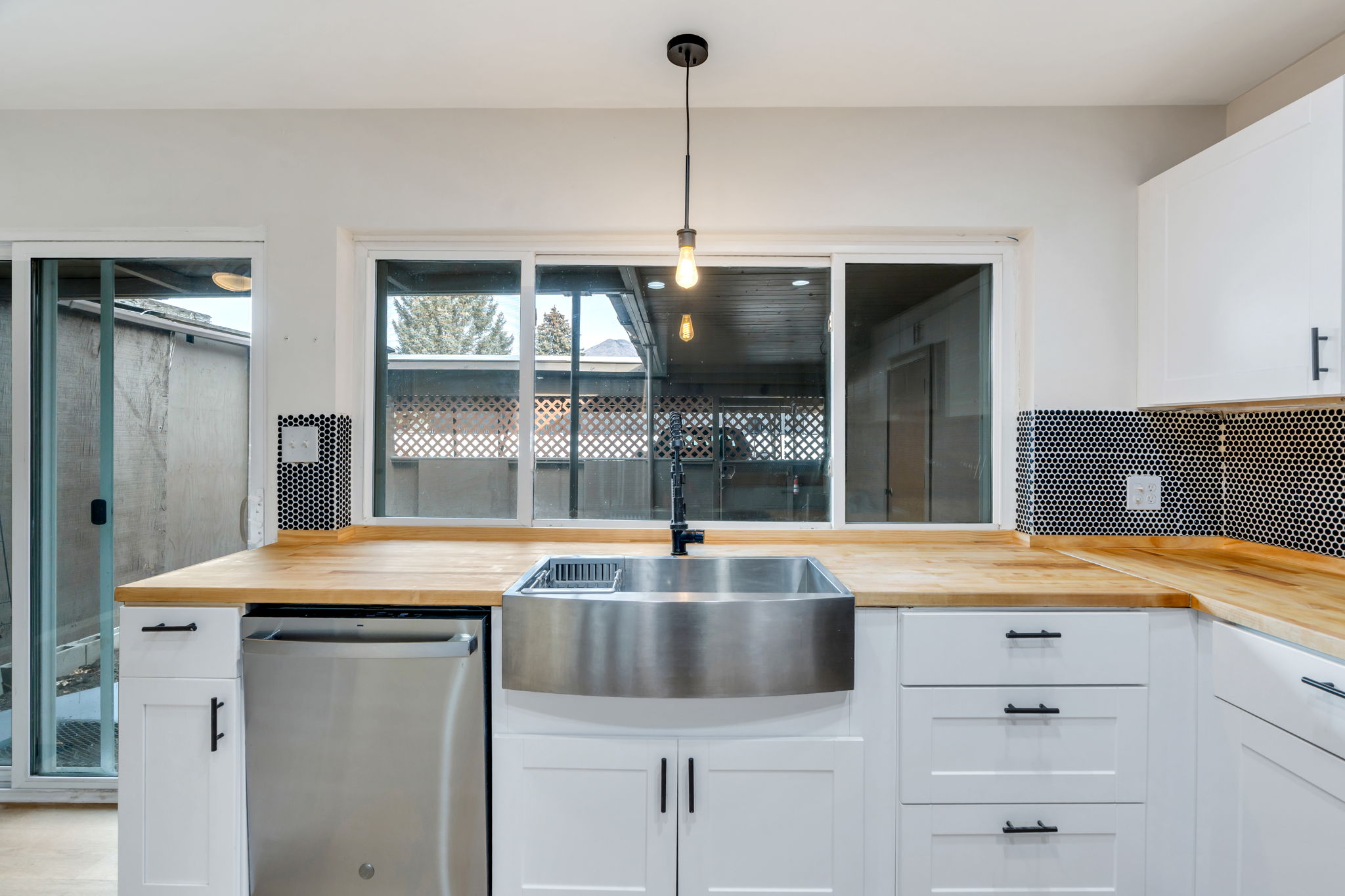 Kitchen featuring white cabinets, wood counters, stainless steel dishwasher, and hanging light fixtures