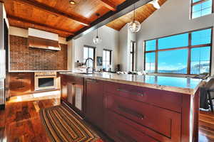 Kitchen featuring hanging light fixtures, light stone countertops, dark wood-type flooring, wall chimney exhaust hood, and open floor plan