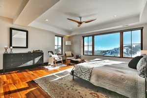 Bedroom with a tray ceiling, hardwood / wood-style floors, a ceiling fan, recessed lighting, and a mountain view