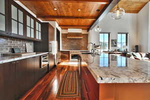 Kitchen with light stone countertops, pendant lighting, dark wood finished floors, decorative backsplash, and a wooden ceiling with exposed beams