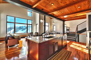 Kitchen featuring open floor plan, light stone countertops, hanging light fixtures, dark wood finished floors, and an island with sink