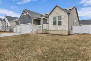 View of front facade featuring roof mounted solar panels, stone siding, a gate, concrete driveway, and board and batten siding