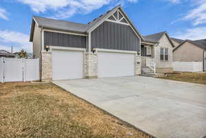 View of front of property with stone siding, board and batten siding, a gate, and concrete driveway