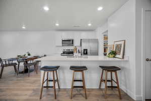 Kitchen featuring a kitchen breakfast bar, light wood-style flooring, white cabinetry, a peninsula, and recessed lighting