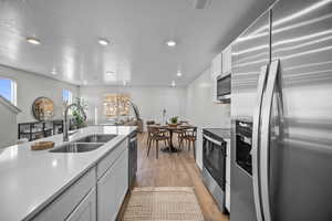 Kitchen featuring stainless steel appliances, white cabinets, light wood finished floors, recessed lighting, and open floor plan