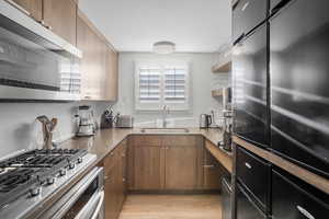 Kitchen featuring stainless steel appliances, open shelves, light wood-type flooring, and light stone countertops