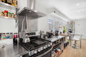 Kitchen featuring stainless steel countertops, gas stove, wall chimney exhaust hood, open shelves, and recessed lighting