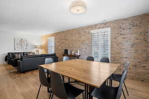Dining room featuring light wood finished floors, healthy amount of natural light, and brick wall