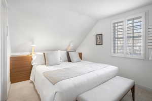 Bedroom with vaulted ceiling and light carpet