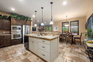 Kitchen with dark brown cabinetry, stainless steel appliances, hanging light fixtures, a kitchen island with sink, and recessed lighting
