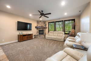 Carpeted living room featuring ceiling fan and a stone fireplace