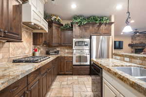 Kitchen featuring dark brown cabinets, stainless steel appliances, hanging light fixtures, custom range hood, and recessed lighting