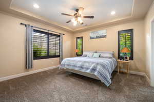 Carpeted bedroom with a raised ceiling, ceiling fan, and recessed lighting