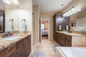 Ensuite bathroom with two vanities, a relaxing tiled tub, and light tile patterned floors