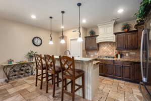 Kitchen with a breakfast bar area, dark brown cabinets, an island with sink, stone tile flooring, and recessed lighting