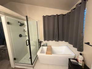 Bathroom featuring a shower stall, a freestanding bath, tile patterned flooring, and lofted ceiling