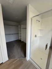 Bathroom with a spacious closet, a shower stall, light wood-style floors, and a textured ceiling