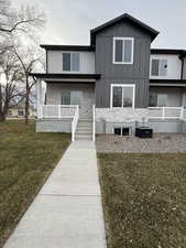 View of front facade featuring a front yard, stone siding, board and batten siding, and covered porch