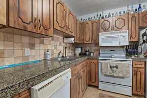 Kitchen with white appliances, tile countertops, brown cabinets, and backsplash