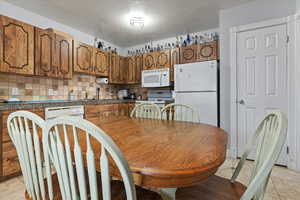 Kitchen featuring white appliances, brown cabinets, a textured ceiling, decorative backsplash, and light tile patterned floors