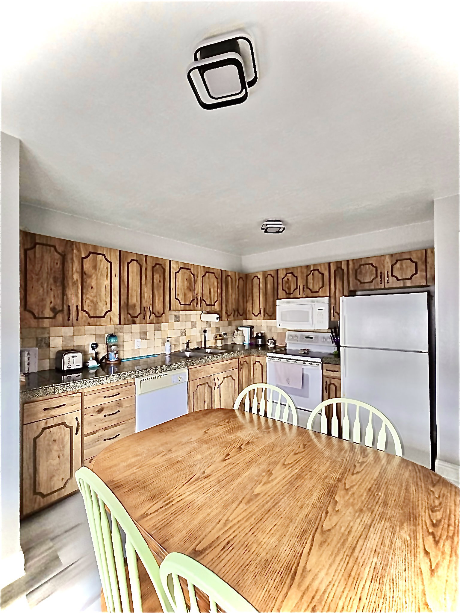 Kitchen featuring white appliances, dark stone counters, wood finish cabinetry, and decorative backsplash