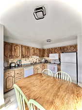 Kitchen featuring white appliances, dark stone counters, wood finish cabinetry, and decorative backsplash