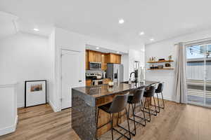 Kitchen featuring dark stone counters, stainless steel appliances, a breakfast bar area, brown cabinets, and light wood-style flooring
