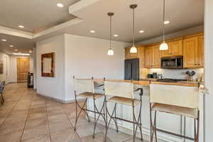 Kitchen featuring recessed lighting, light stone countertops, hanging light fixtures, a breakfast bar, and high end black refrigerator