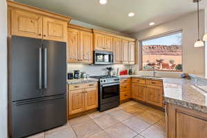Kitchen with freestanding refrigerator, stainless steel gas stove, pendant lighting, recessed lighting, and light stone countertops