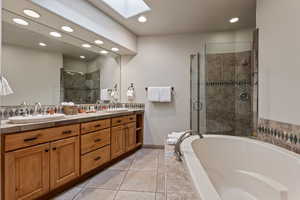 Full bathroom featuring double vanity, a skylight, a bath, a shower stall, and recessed lighting